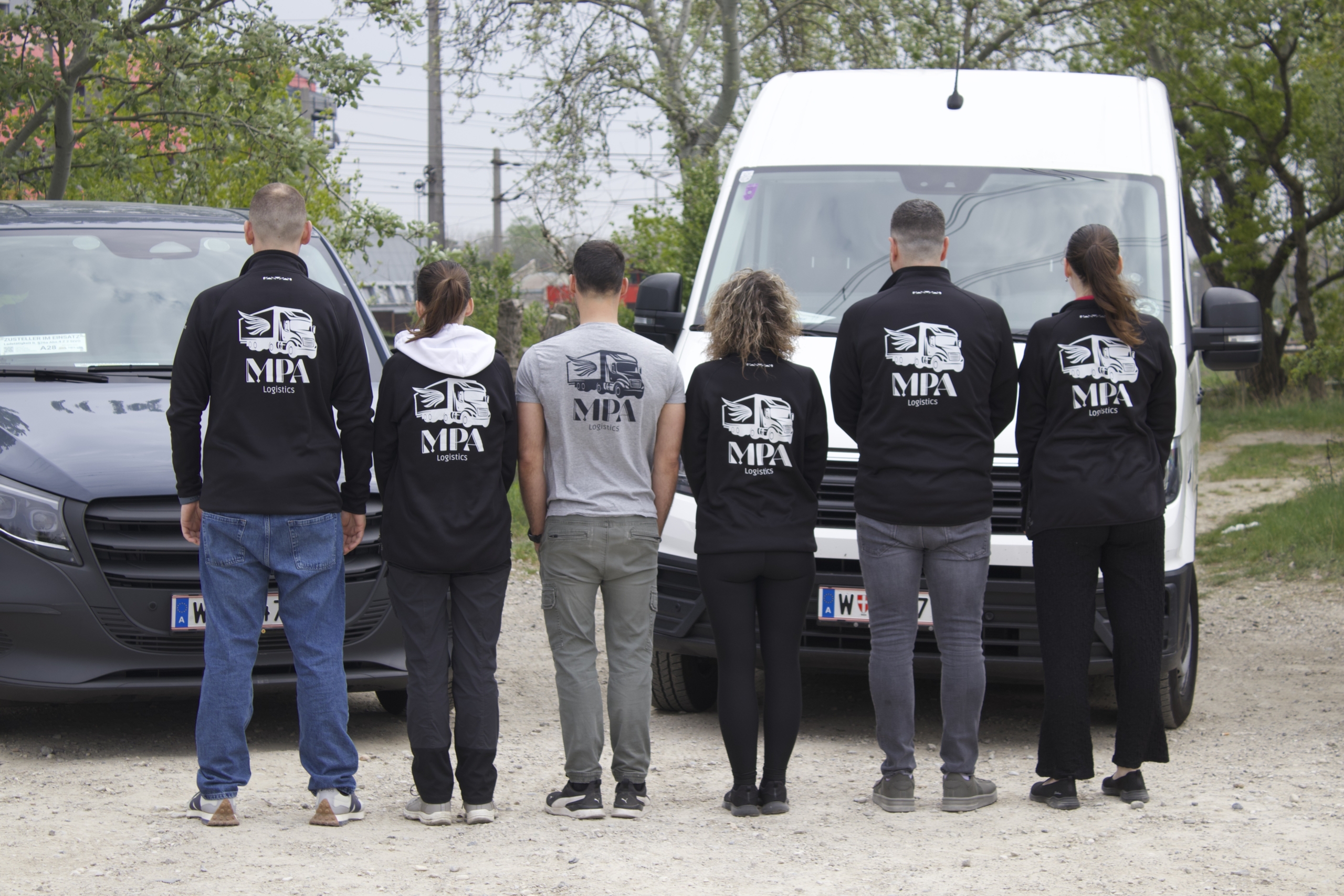Ein Foto der Mitarbeiter der MPA Logistics mit dem Rücken zu Kamera. Hinter Ihnen sind Lieferwagen zu sehen.